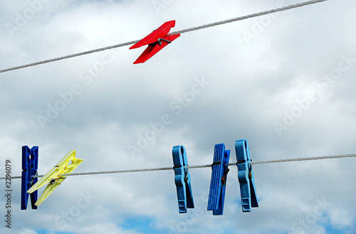 Clothes pegs on a wire with clouded sky as background. Blue white yellow red. Copy space.