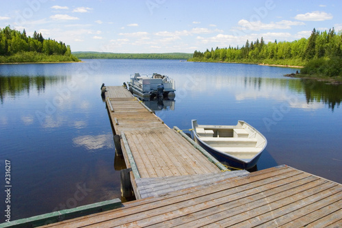 Fototapeta Naklejka Na Ścianę i Meble -  two boats docked on a peaceful lake on a sunny day with trees and blue water behind