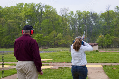woman shooting skeet with a range safety officer standing next to her