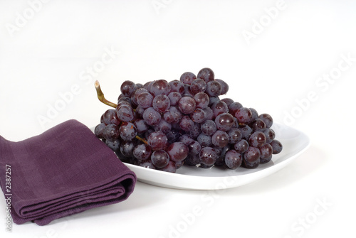 a bunch of juicy red grapes on a white plate with a purple napki photo