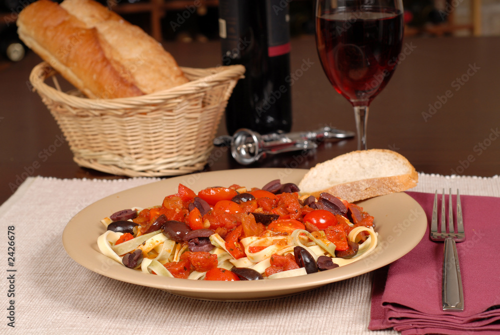 a plate of pasta puttanesca with wine and bread
