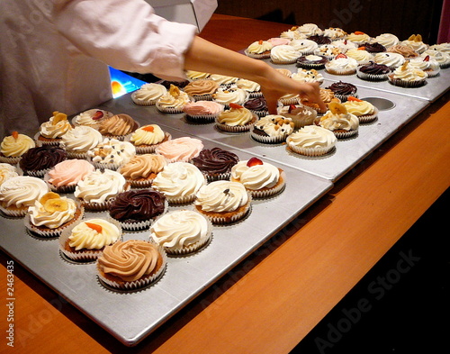 baker reaches for cupcake in gourmet bakery photo