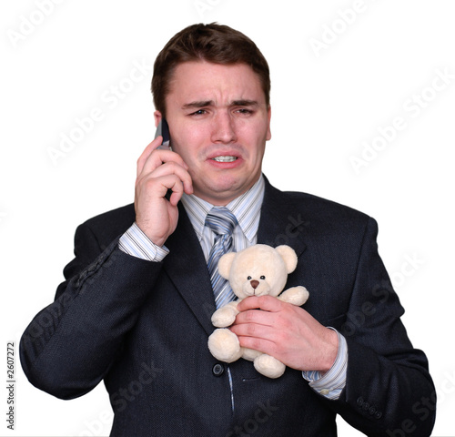 young businessman crying on cell phone, clutching teddy bear. photo