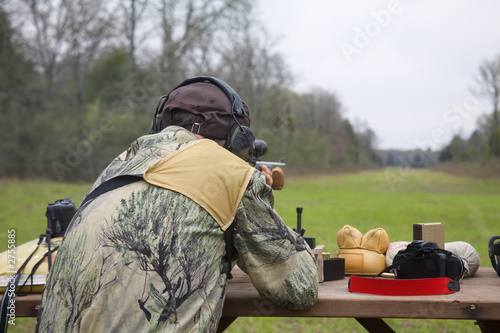 shooter at the bench sighting in a long-range rifle at an outdoor range covered in grass.