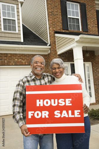 middle-aged couple holding a for sale sign.