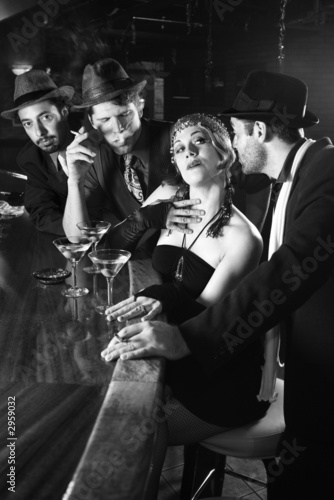 retro female sitting at bar surrounded by men.