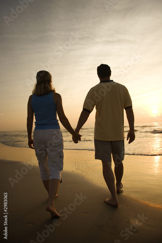 Couple walking on beach at sunset. © iofoto