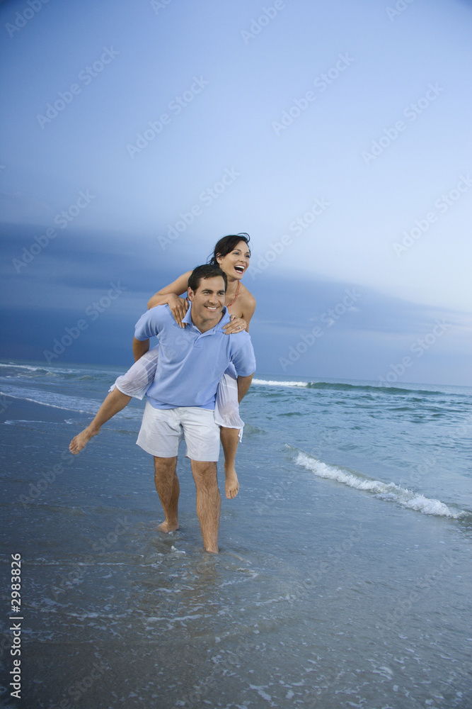 Man carrying woman piggyback at beach.