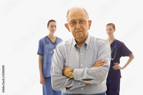 elderly man in foreground with two nurses in background.