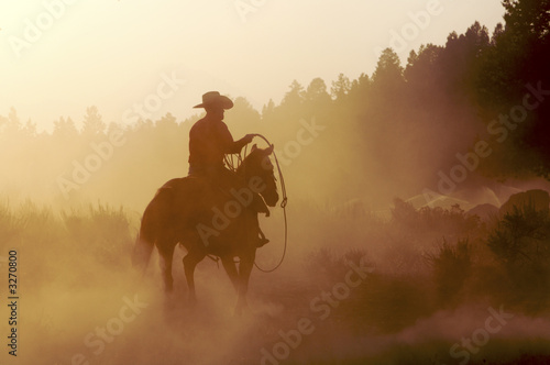 Silhouette of cowboy riding horse at sunset photo