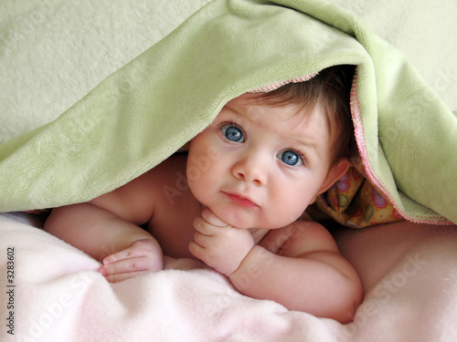 beautiful baby looking out from under blanket