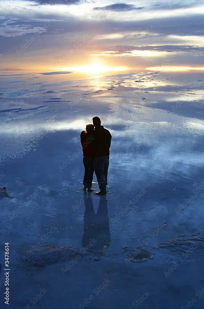 couple watching sunset over wet salt flats couple watching sunset over wet salt flats