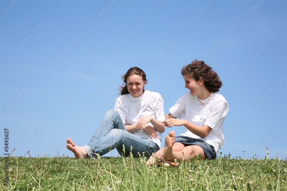Two girlfriends in white T-shorts have a rest on a grass Two girlfriends in white T-shorts have a rest on a grass