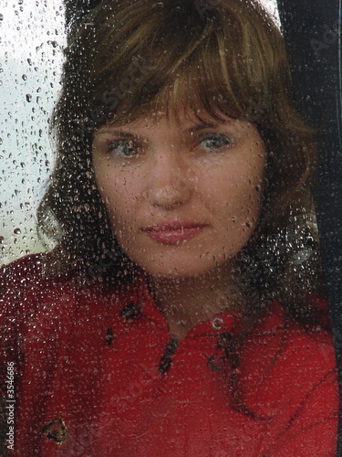 Girl looks thru waterdropped widow glass in rainy weather