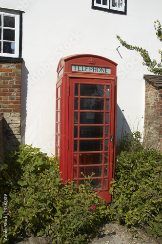 An old red telephone box by a white wall
