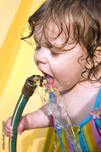 a toddler drinking water from a garden hose