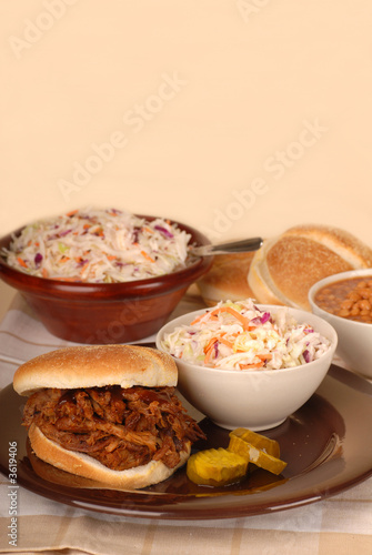 A pulled pork sandwich with cole slaw, baked beans and pickles