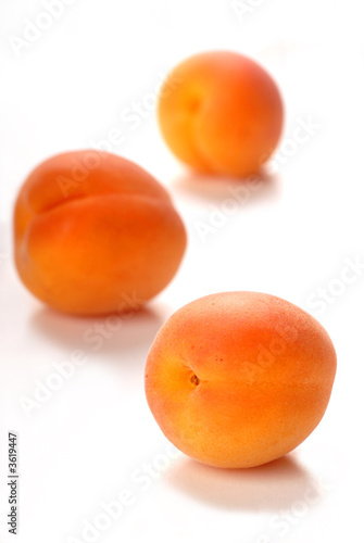Three apricots on a white surface with a shallow depth of field