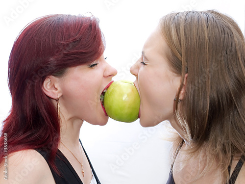 Two girls bite a green apple
