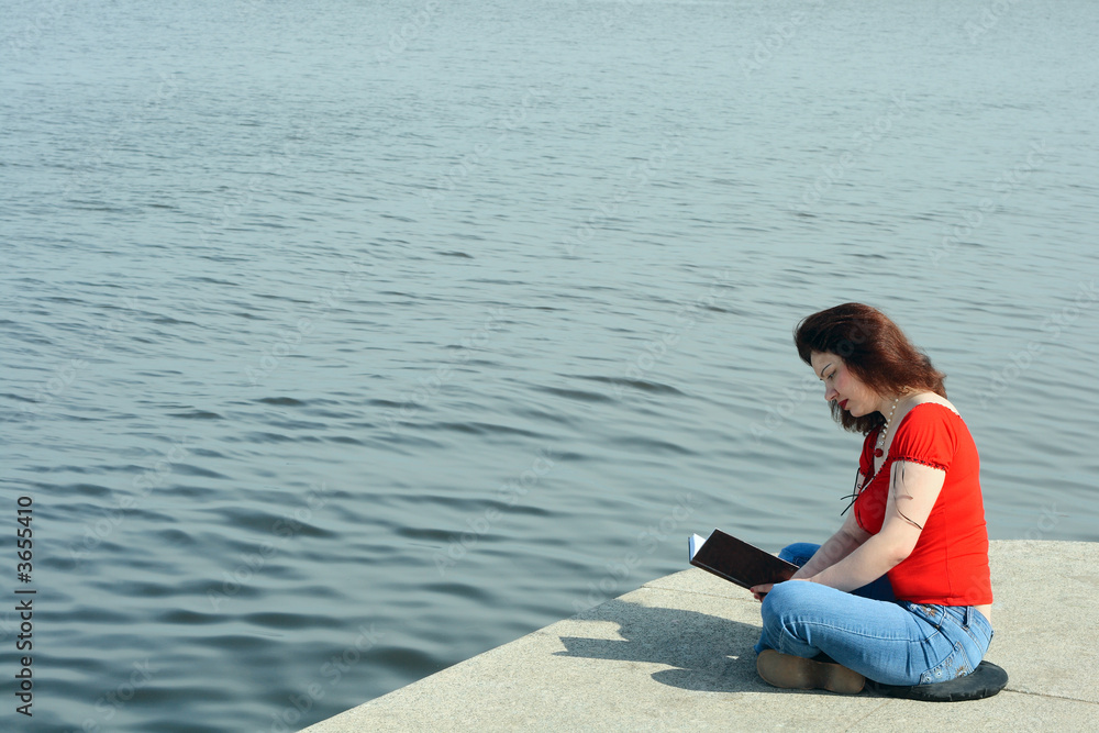 Woman sitting and reading on sea embankment