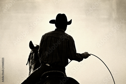 Vászonkép cowboy at the rodeo - shot backlit against dust, added grain