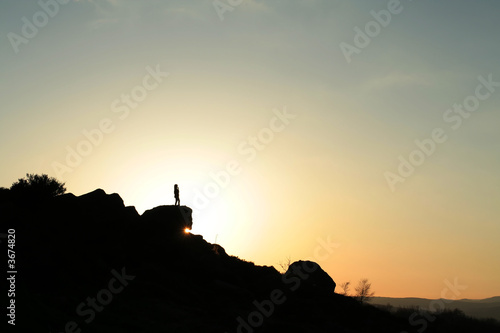 Girl silhouetted against the setting sun,stood on rock outcrop
