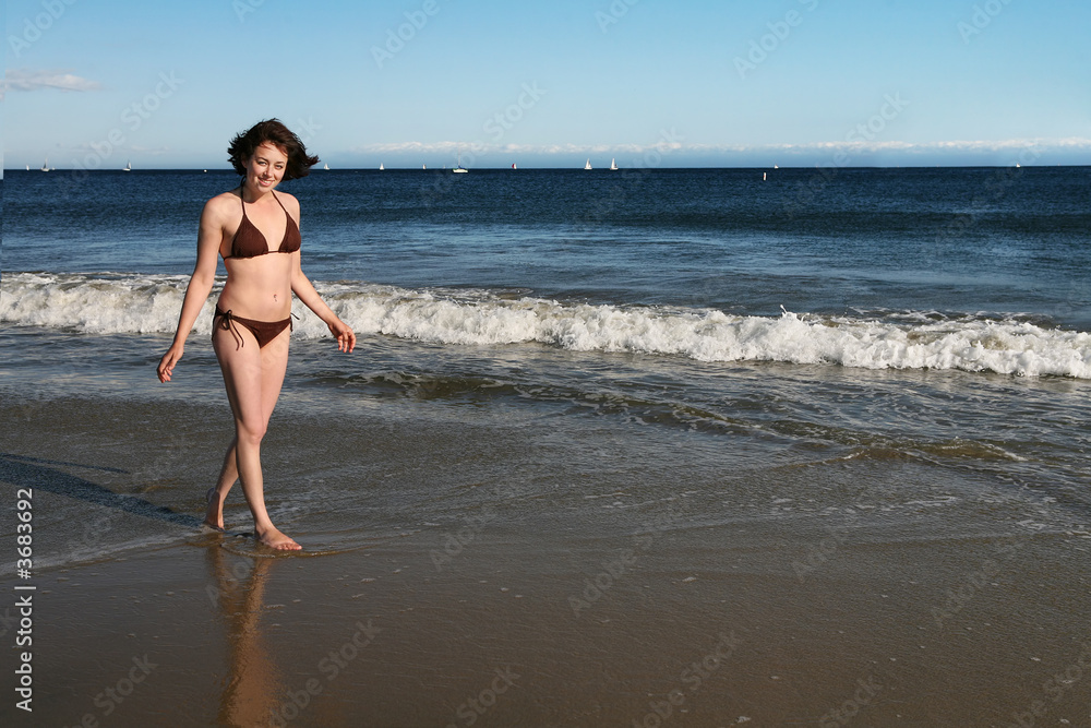 A pretty woman walking on the beach near the water A pretty woman walking on the beach near the water