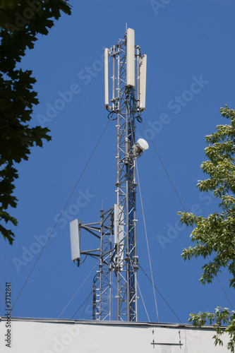 Two masts with cell antennas on a roof, against blue sky