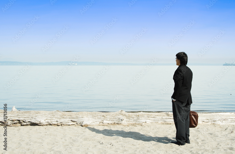 A businessman standing on the beach alone enjoying the view A businessman standing on the beach alone enjoying the view