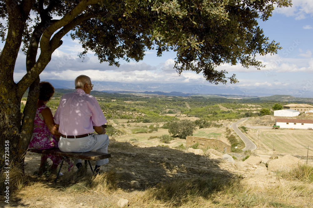 Old couple sitting on a bench, watching at the landscape