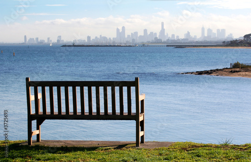 Park bench on a clifftop, overlooking a bay to city skyline 