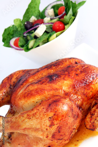 Golden roasted chicken with Greek salad behind.