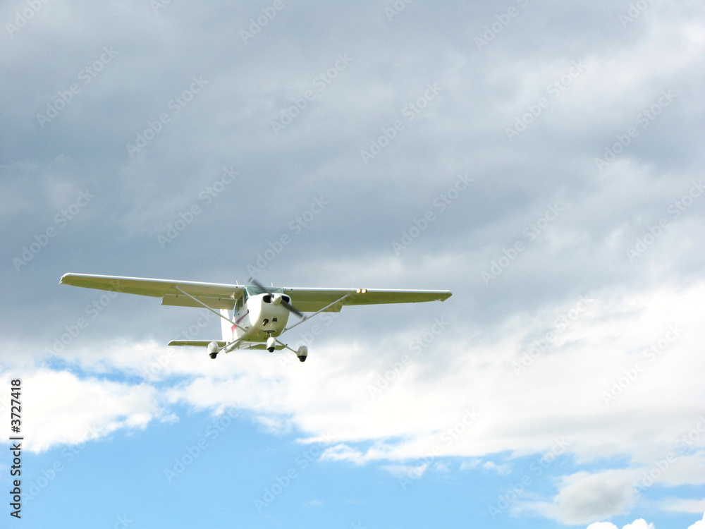 weisses Sportflugzeug fliegt durch blauen und wolkigen Himmel