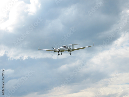 weisses Sportflugzeug fliegt durch blauen und wolkigen Himmel