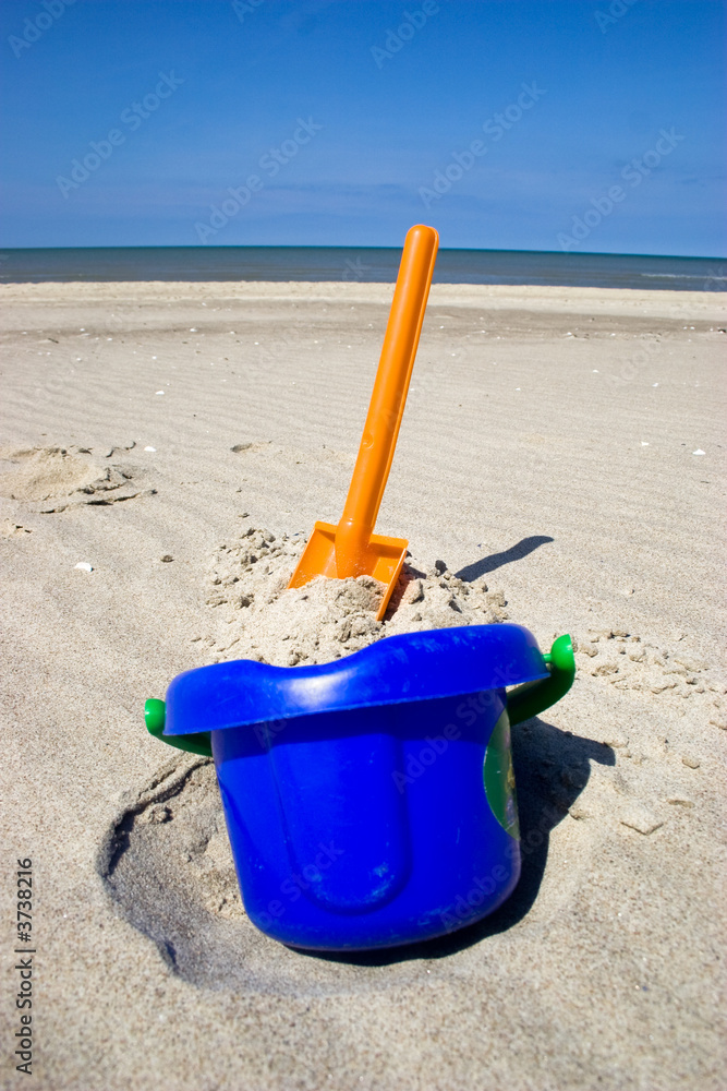 Orange plastic spade and blue bucket in the sandy seashore Orange plastic spade and blue bucket in the sandy seashore