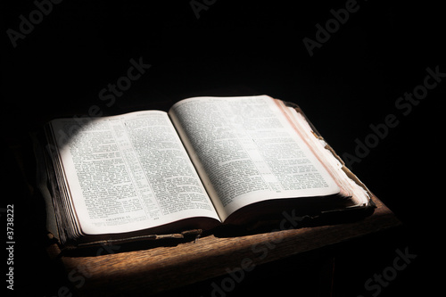 Old open bible lying on a wooden table in a beam of sunlight 