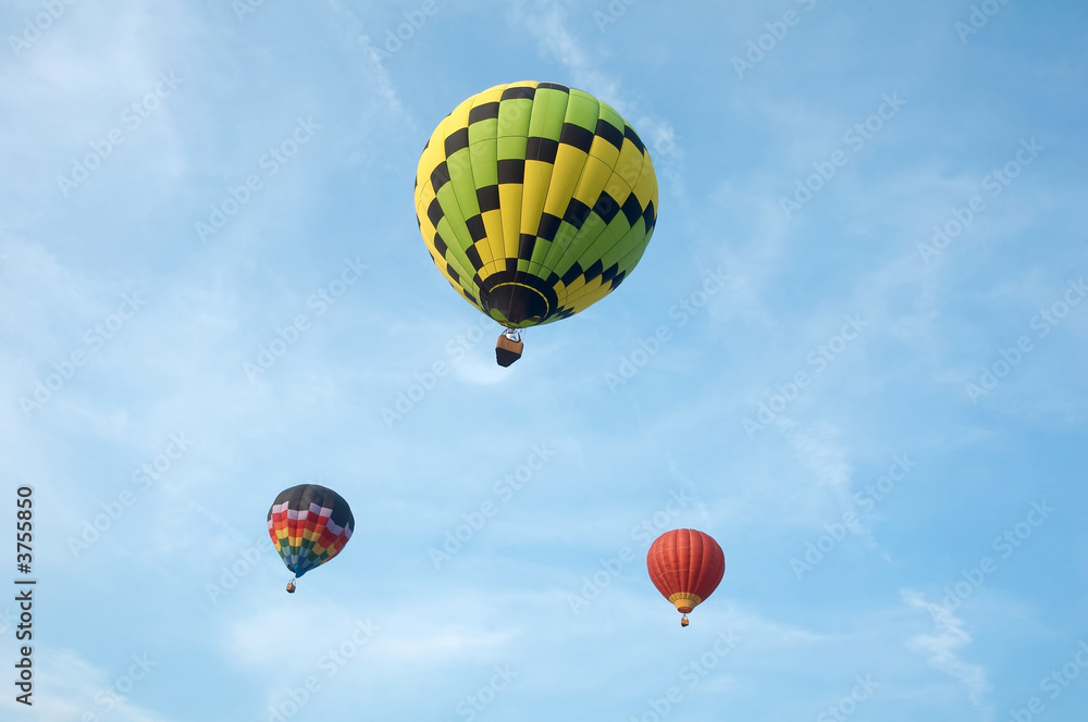 Fototapeta premium Three hot air balloons floating in a cloudy sky.