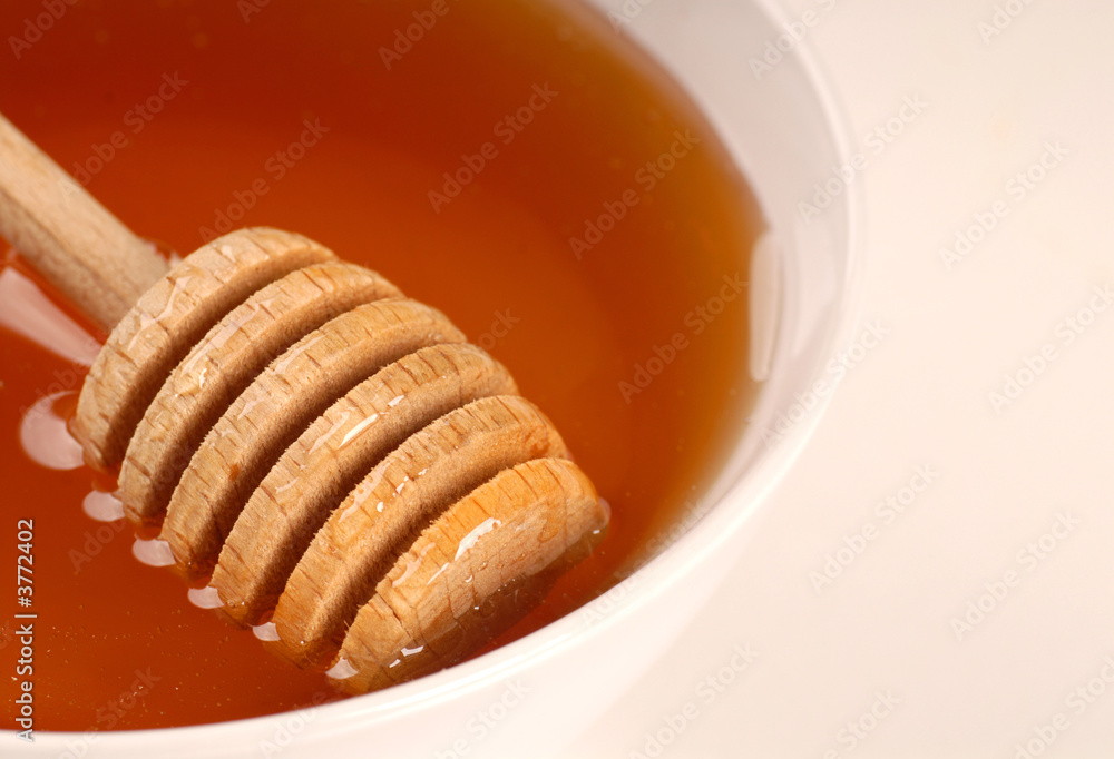 A closeup of a bowl of amber honey with a honey wand A closeup of a bowl of amber honey with a honey wand