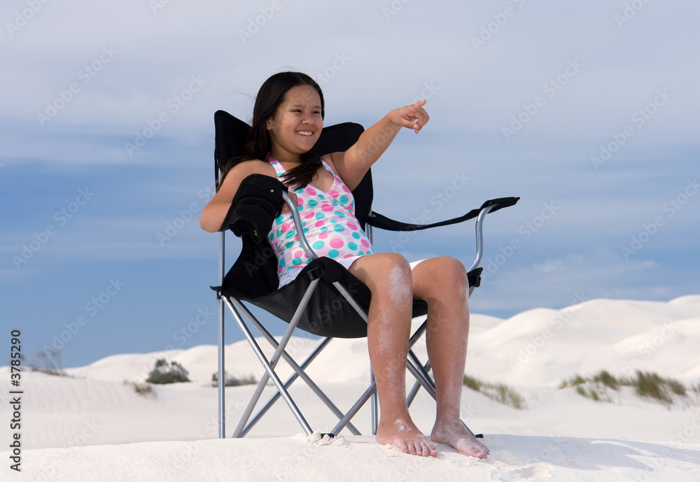 girl sitting in beach chair pointing to distance 