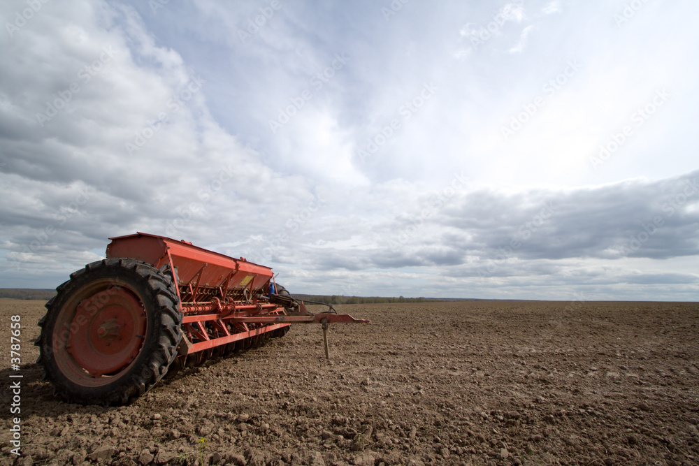Fototapeta premium Seeding machines at field and sky with clouds.