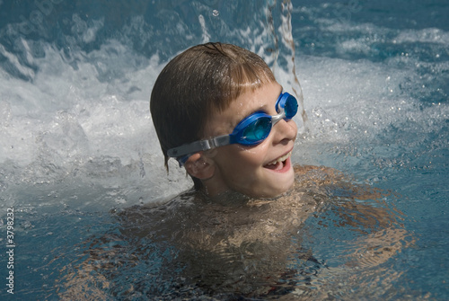 Kind mit Schwimmbrille lacht im Wasserfall eines Freibades