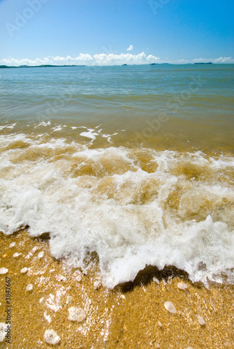 A wave and surf reaches the shore of a sandy beach photo