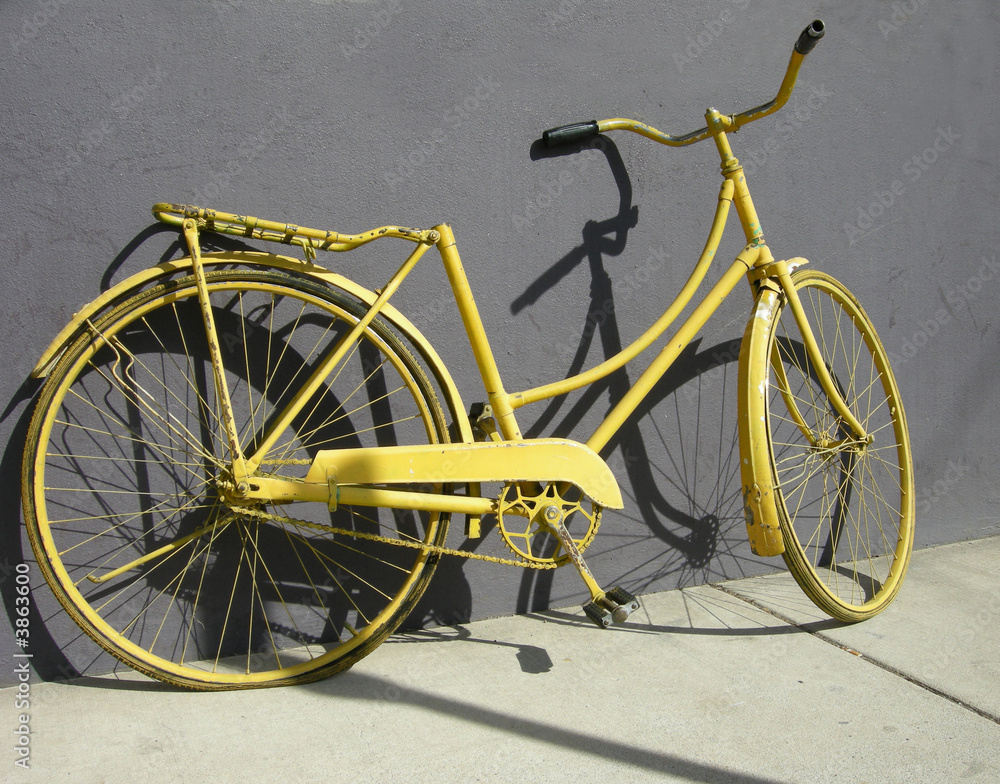An old yellow bike leaning on a grey wall An old yellow bike leaning on a grey wall