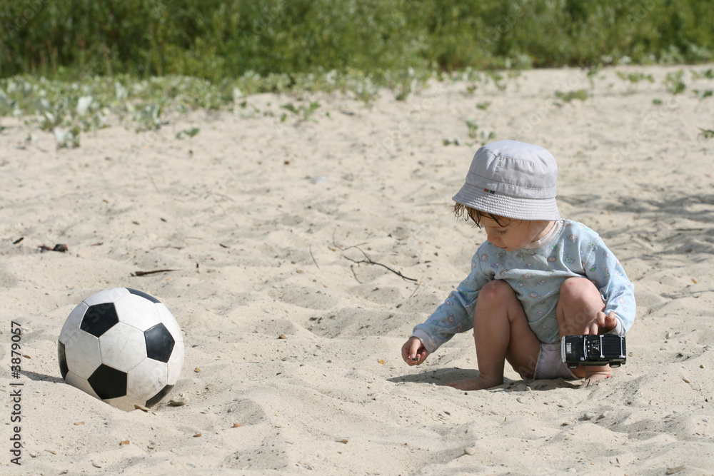 boy plays on sand with the toy automobile near to a football boy plays on sand with the toy automobile near to a football