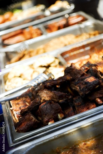 Trays of juicy barbecue food, focus on ribs in front