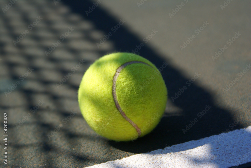 Tennis ball laying in the shadow of tennis net