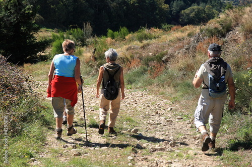 Trois marcheurs, un homme et deux femmes, randonnent sur un chemin caillouteux