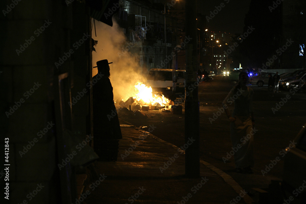 silhouette of hasidic jew standing in front of  riot fires