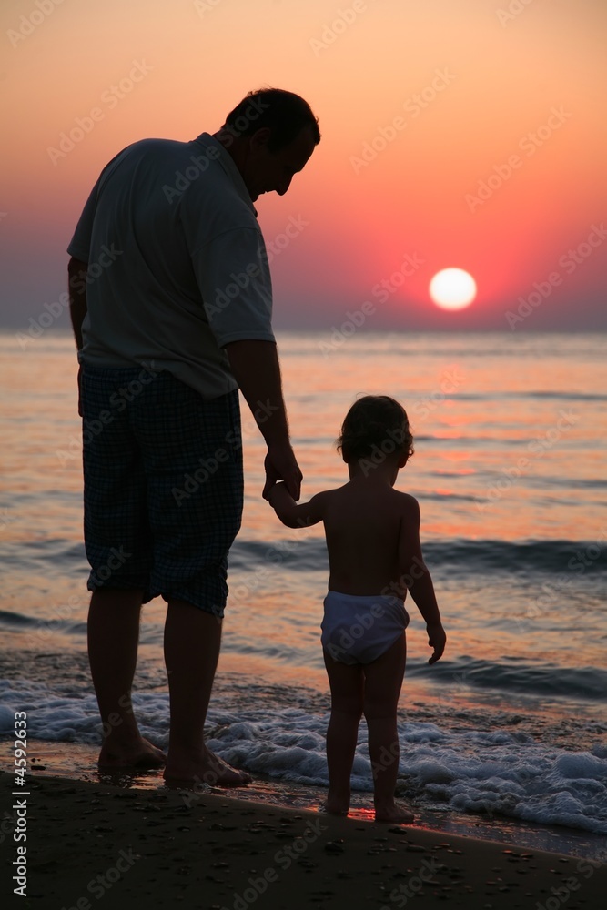 Grandfather with child on sunset at sea 