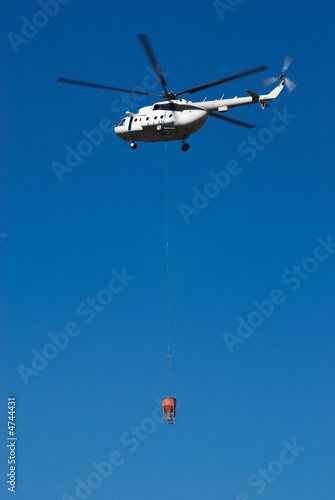 Fly big white helicopter with cargo on rope